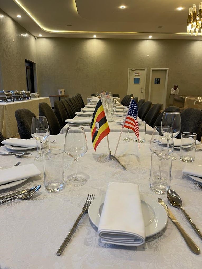 A conference room with tables set for a meeting, flags of the United States and Rwanda, and a person standing by the door.