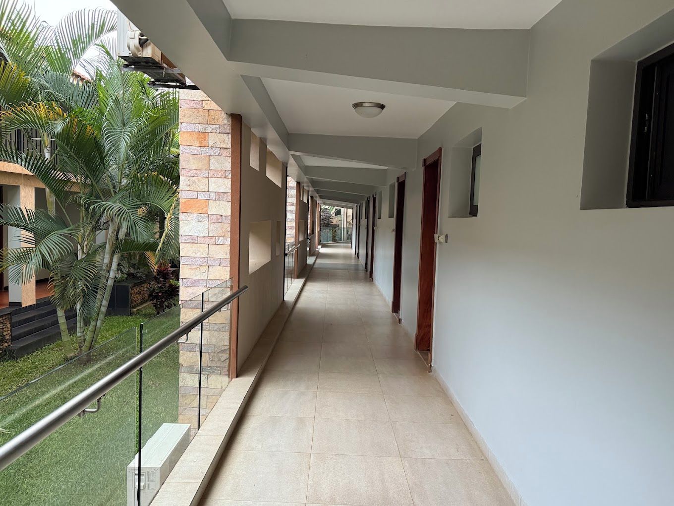 A corridor with a glass balustrade, tiled flooring, and a view of greenery outside.