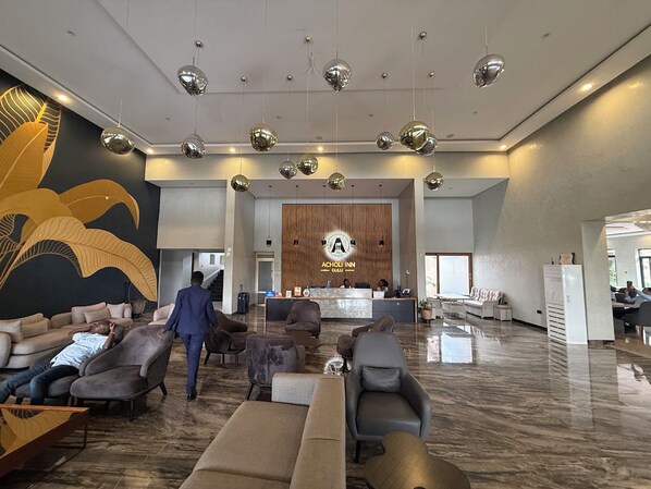 Un vestíbulo de hotel con mostrador de recepción, zona de estar y un gran elemento decorativo en la pared.