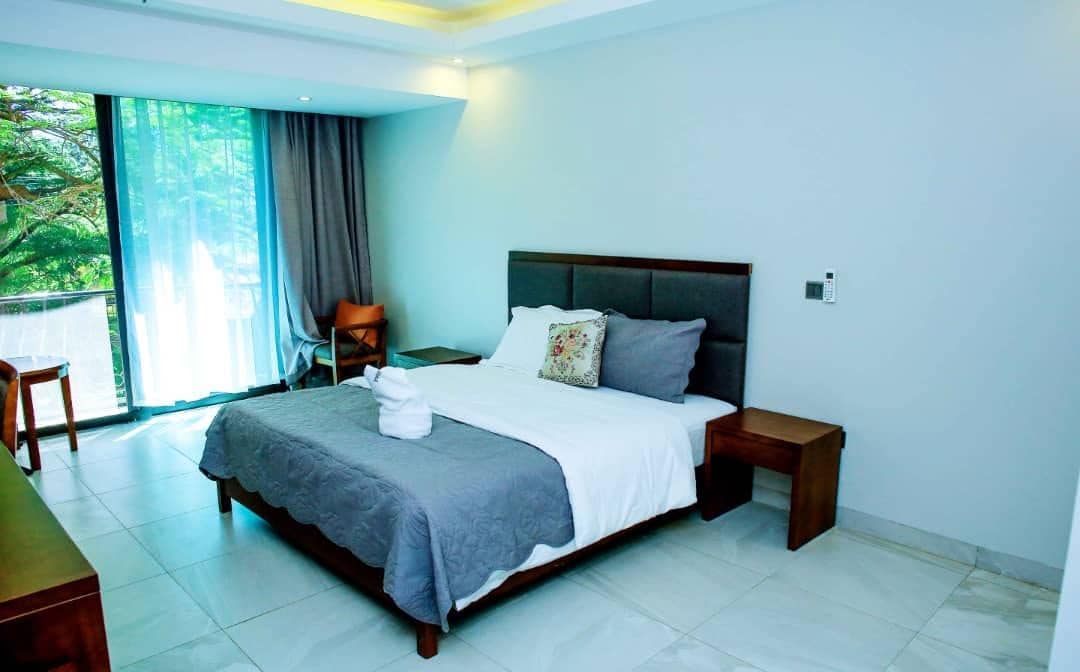 Habitación de hotel con una cama grande, una mesita de noche, una silla y vistas al exterior.