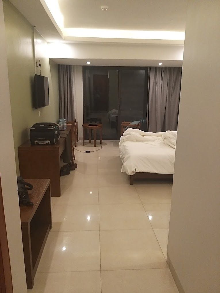 Una habitación de hotel con cama, escritorio, silla, televisor y puerta corrediza que da a un balcón.