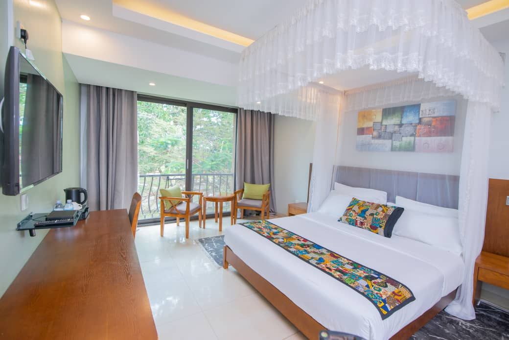 A hotel room with a large bed, a wooden desk, a television, and a balcony with chairs.