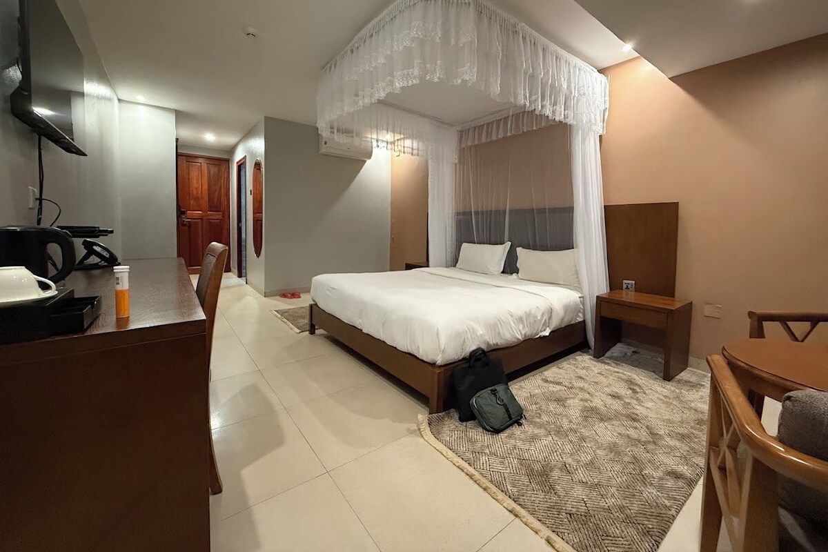 Una habitación de hotel con cama, mesita de noche, silla, escritorio y televisor.