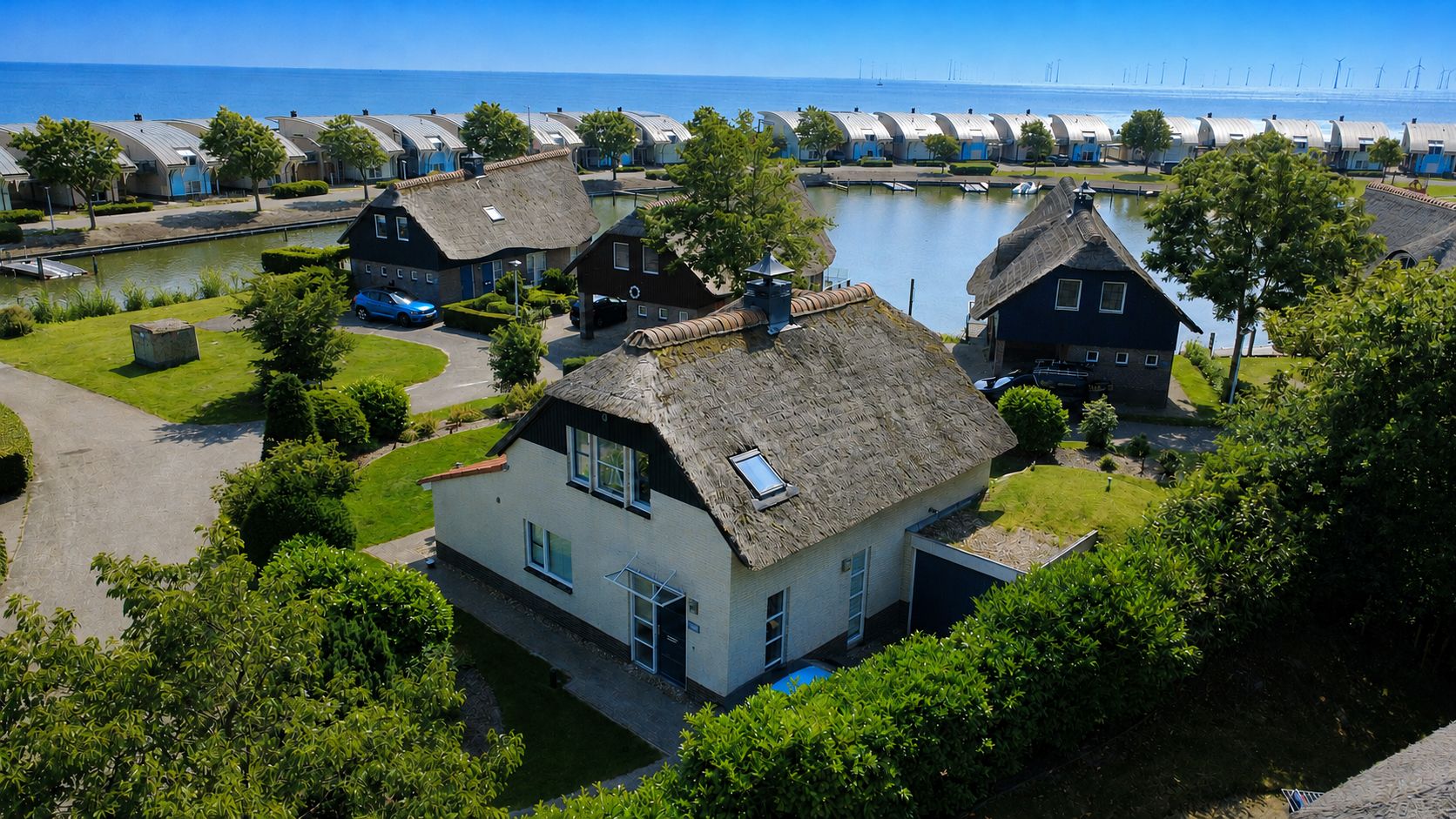 A coastal village with traditional thatched-roof houses, a calm lake, and a clear view of the sea.