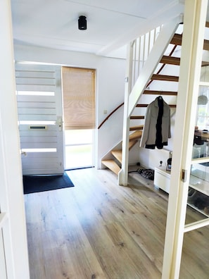 Un intérieur moderne avec un escalier en bois, un manteau accroché à la rampe et une porte donnant sur un espace extérieur.