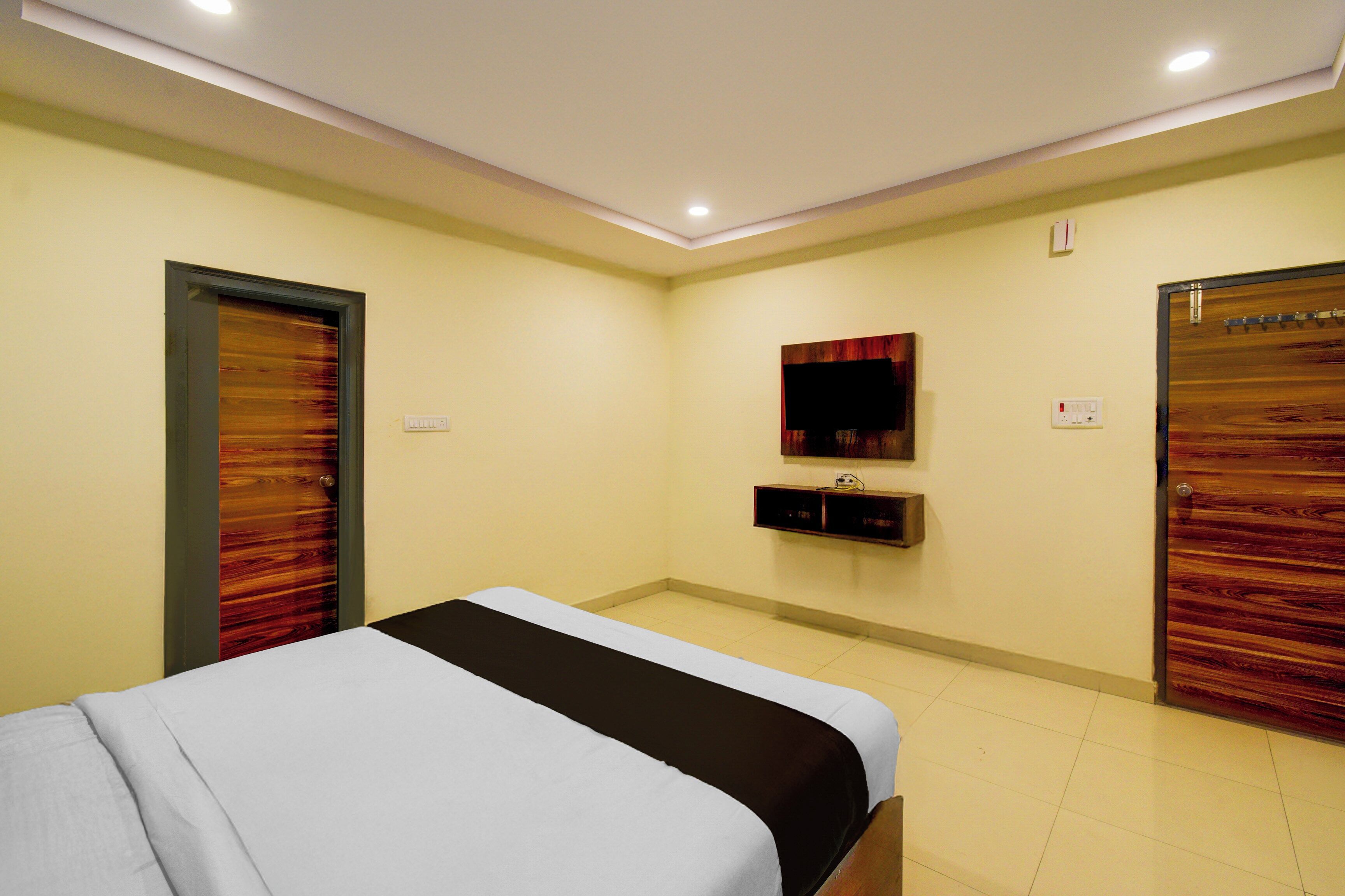 Habitación de hotel con cama, puertas de madera, televisor montado en la pared y una pequeña estantería.