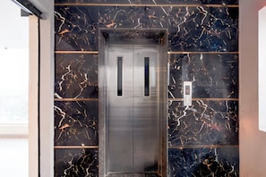 An elevator with a metallic finish, set against a wall with a black and gold marble pattern. - Super Hotel O AMR Planet Mall Hyderabad (Hyderabad)