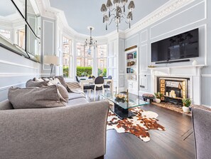 A modern living room with a sofa, a glass coffee table, a fireplace, and a TV mounted on the wall. - Lovely Flat near Royal Botanic Garden (Edinburgh)