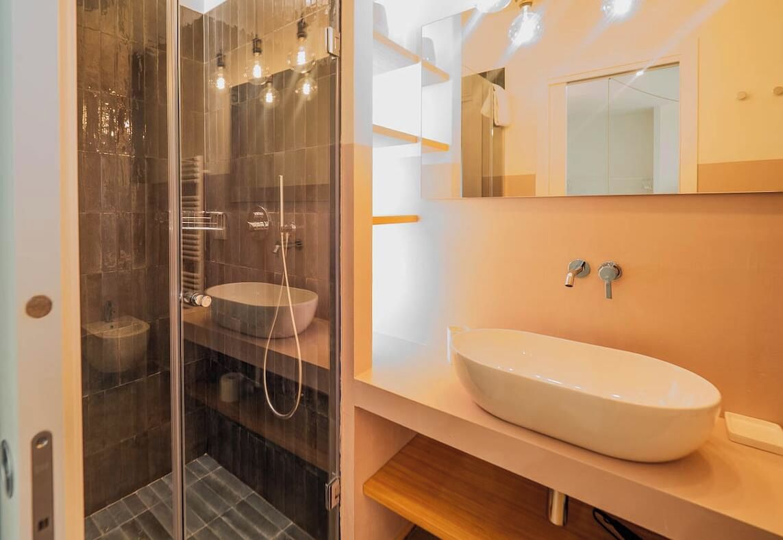 Une salle de bain moderne avec une douche en verre, un lavabo blanc et un miroir au-dessus du lavabo.