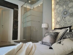 A modern bedroom with a glass shower enclosure, a bed with white bedding, and a wall with a decorative plate pattern. - Vernazza Luxury Apartment with AC (Vernazza)