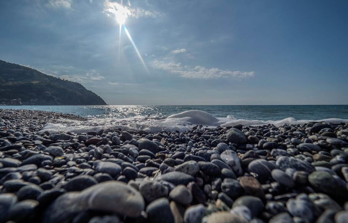 Ein felsiger Strand mit Wellen, einem klaren Himmel und einer strahlenden Sonne.