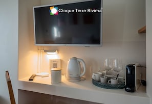 Una TV a schermo piatto montata sopra un bancone bianco, con un telecomando, una tazza, un bollitore ed una macchina da caffè Krups.