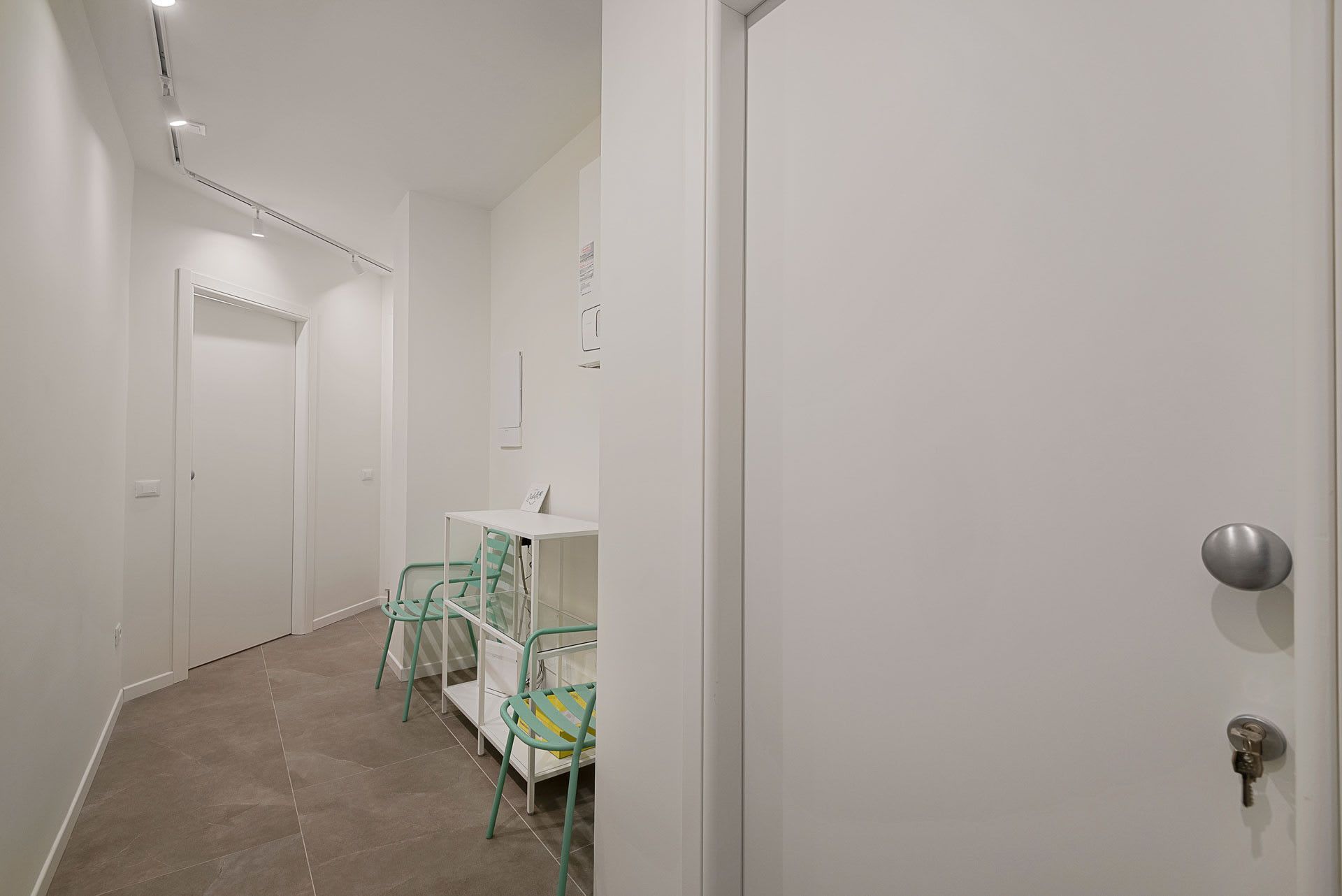 Ein Flur mit einer weißen Tür, einem kleinen Tisch mit Stühlen und einer Leuchte an der Decke.