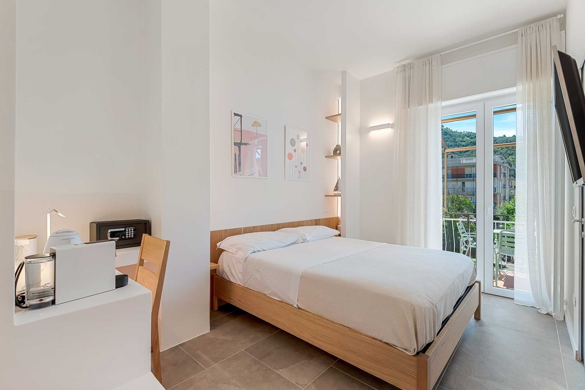 Ein Schlafzimmer mit einem Bett, einem Schreibtisch mit Computer, einem Stuhl, einem Fenster mit Vorhängen und einem Balkon mit Blick.