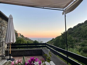 A balcony with a view of the sea and hills, a white umbrella, and a flower arrangement. - Villa Olive Mill Terra Rossa (Corniglia)