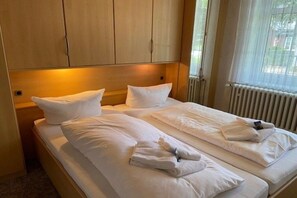 A hotel room with a double bed, two pillows, a headboard, and a window with blinds. - Holiday apartment with 1 bedroom (Wyk auf Föhr)