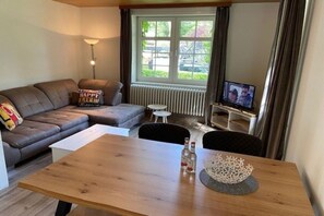 A living room with a sofa, a coffee table, a TV, and a window with curtains. - Holiday apartment with 1 bedroom (Wyk auf Föhr)
