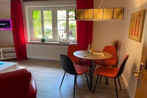 Ein Essbereich mit einem runden Tisch, vier Stühlen, einem Heizkörper, einem Fenster mit Vorhängen und einem Fernseher an der Wand.