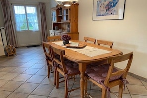 A dining area with a wooden table and chairs, a cabinet, and a window with curtains. - Strandstraße 28, half of the house on the left (Nieblum)