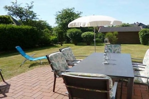 An outdoor patio with a table and chairs, a white umbrella, and a brick floor. - Strandstraße 28, half of the house on the left (Nieblum)