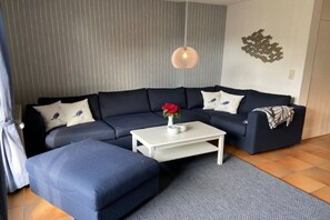 A modern living room with a sectional sofa, a white coffee table, and a decorative wall piece. - Holiday home in Oldsum with swimming pool (Oldsum)