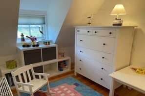 A child's playroom with a white dresser, a rocking chair, and a window with toys on the sill. - Holiday home in Oldsum with swimming pool (Oldsum)