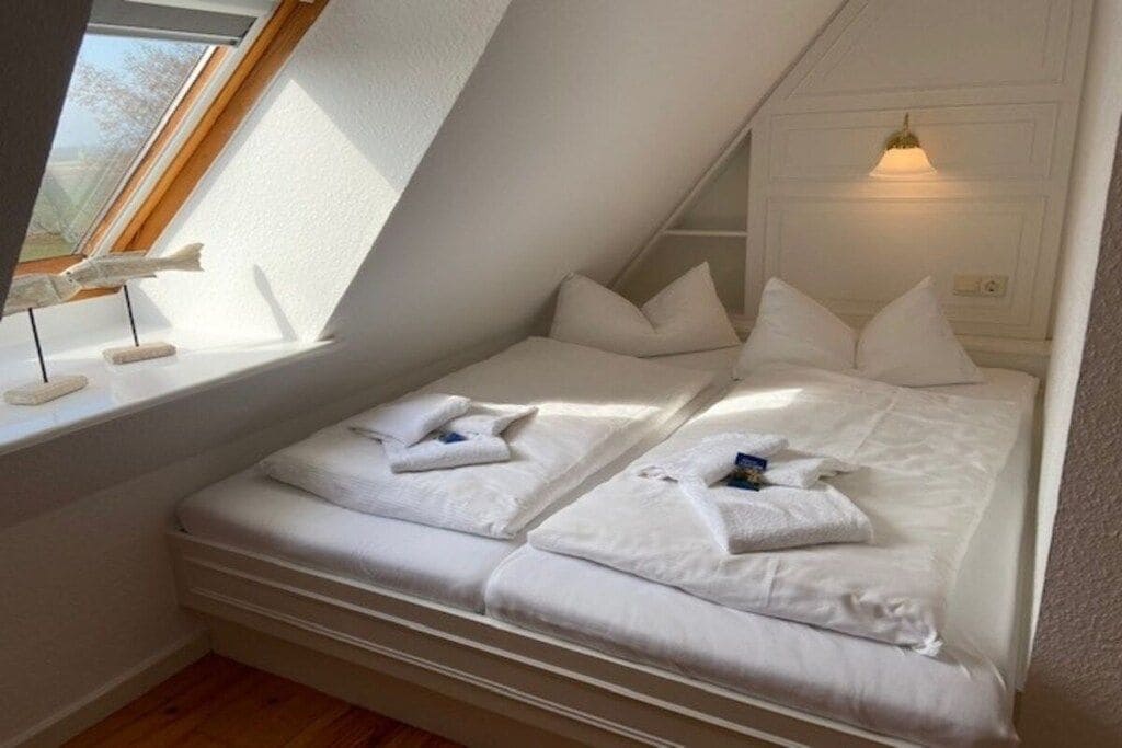 Une petite chambre avec un lit simple, un plafond en pente, une fenêtre donnant sur un beau paysage et un luminaire fixé au mur.