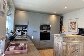 A modern kitchen with grey cabinets, a microwave, an oven, and a wooden counter with a coffee machine. - Holiday home in Nieblum with swimming pool (Nieblum)