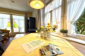 A room with a dining table set for two, a sofa, a television, and a window with curtains. - Holiday apartment with 1 bedroom (Wyk auf Föhr)