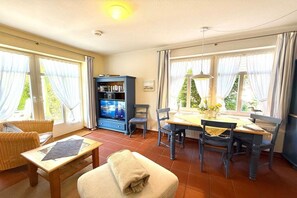 A room with a dining table, chairs, a sofa, a television, and a bookshelf. - Holiday apartment with 1 bedroom (Wyk auf Föhr)