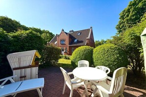 Een terras met een tafel en stoelen, een rieten stoel en een witte ligstoel.