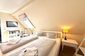A bedroom with two beds, a bedside table with a lamp, a bookshelf, and a window with curtains. - Holiday apartment with 2 bedrooms (Dunsum)