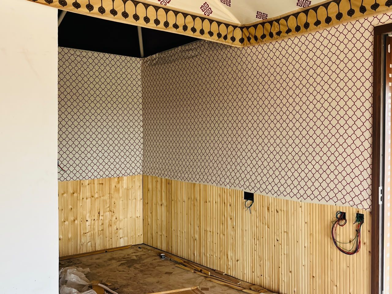 A room with a wooden floor, a patterned wall, and a door.
