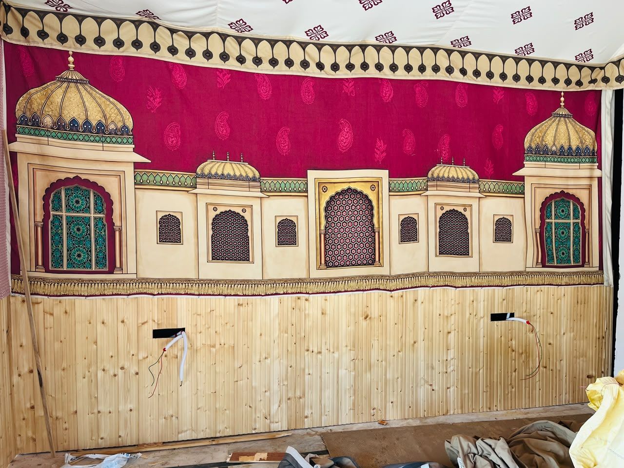 A room with a wooden wall, a red curtain, and a patterned tapestry.