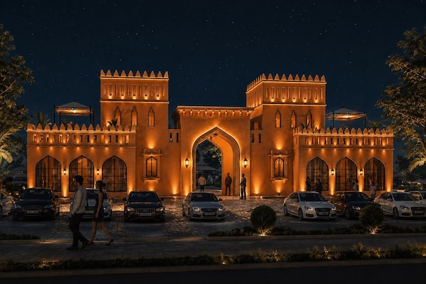 A grand hotel entrance with a large archway, multiple car parking spaces, and a well-lit facade.