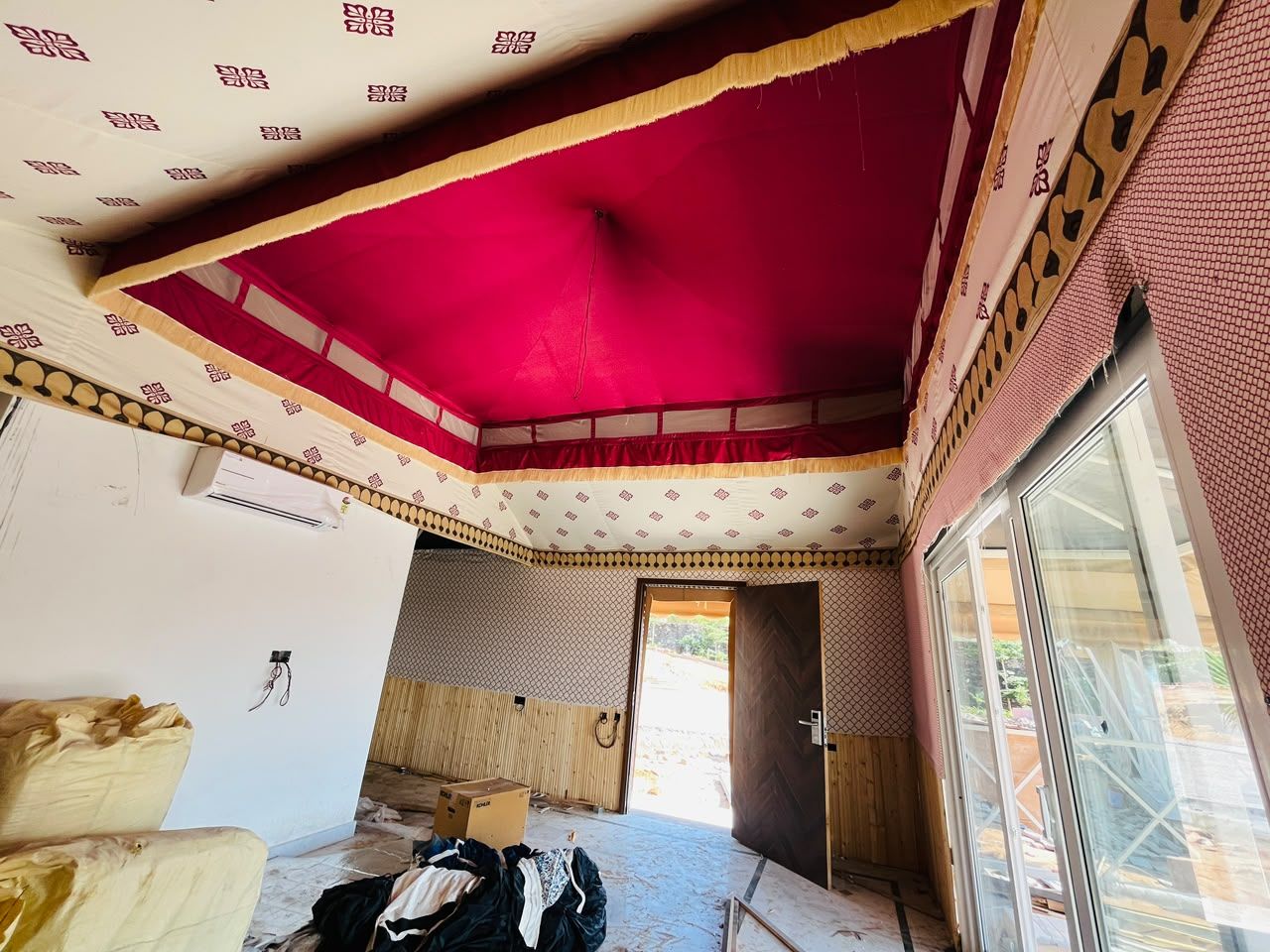 Una stanza con soffitto rosso, parete decorata e un'ampia finestra.