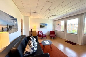 Un intérieur moderne avec un canapé, des fauteuils rouges, une petite table et des œuvres d’art accrochées aux murs.