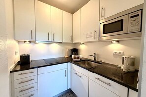 A compact kitchen with white cabinets, a black countertop, a built-in microwave, and a coffee maker. - Holiday apartment with 2 bedrooms (Wyk auf Föhr)
