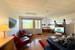 A modern living room with red chairs, a sofa, a TV, and a bookshelf. - Holiday apartment with 2 bedrooms (Wyk auf Föhr)