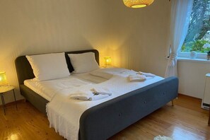 A neatly made bed with white linens and towels, a bedside lamp, and a window with curtains. - Holiday apartment with 2 bedrooms (Midlum auf Föhr)