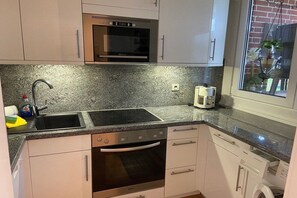 A kitchen with a double sink, a built-in oven, a microwave, and a window with a view of a brick building. - Holiday apartment with 2 bedrooms (Midlum auf Föhr)