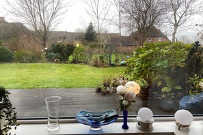 Una finestra amb vista a un jardí, un vas de vidre transparent i un bol de vidre blau.