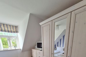 Ein Schlafzimmer mit einem Bett, einem Kleiderschrank, einem Fernseher und einem Fenster mit Blick auf Grünflächen.