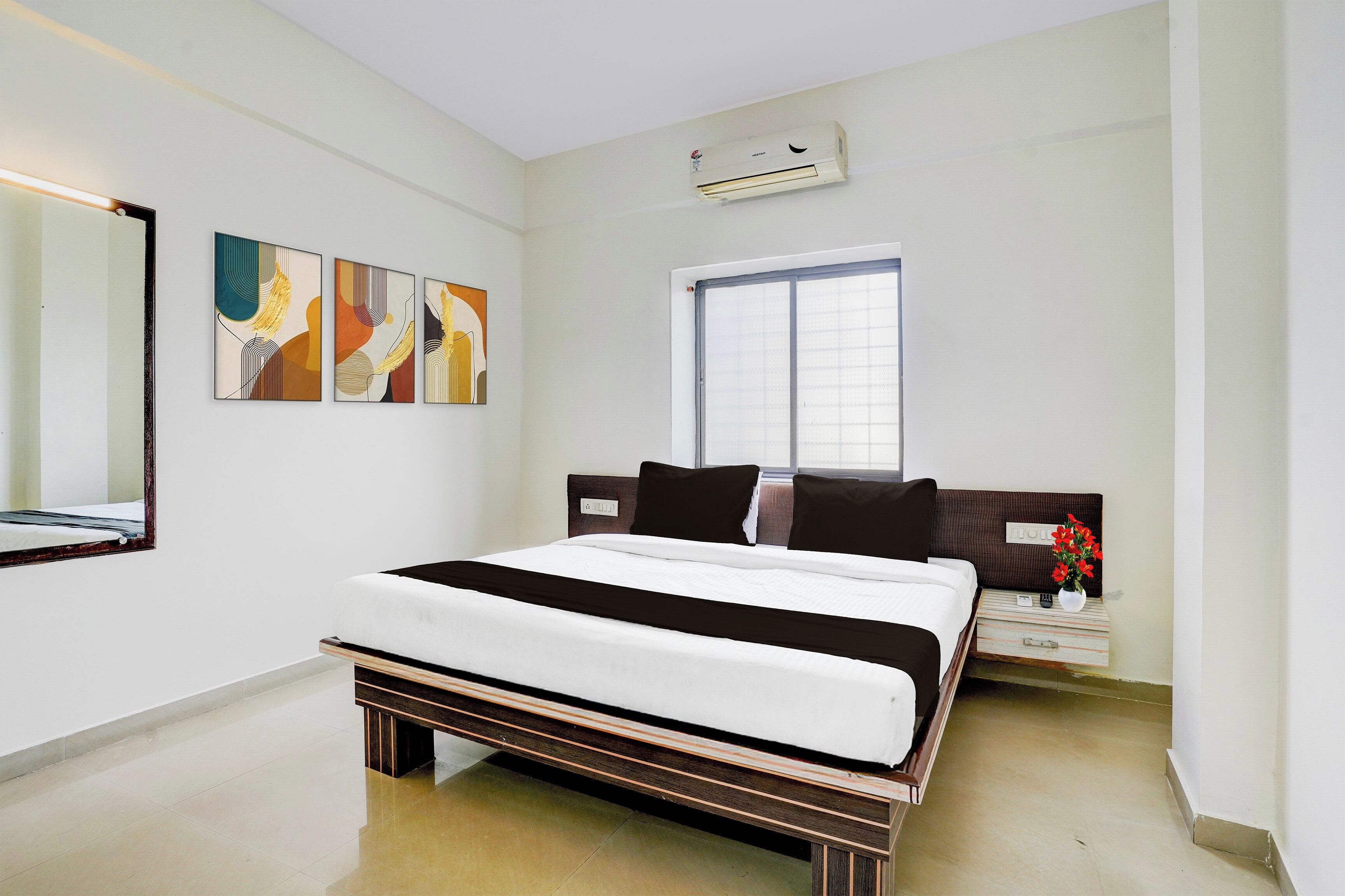 Une chambre d’hôtel avec un lit, une table de chevet, un miroir et des œuvres d’art abstraites accrochées au mur.