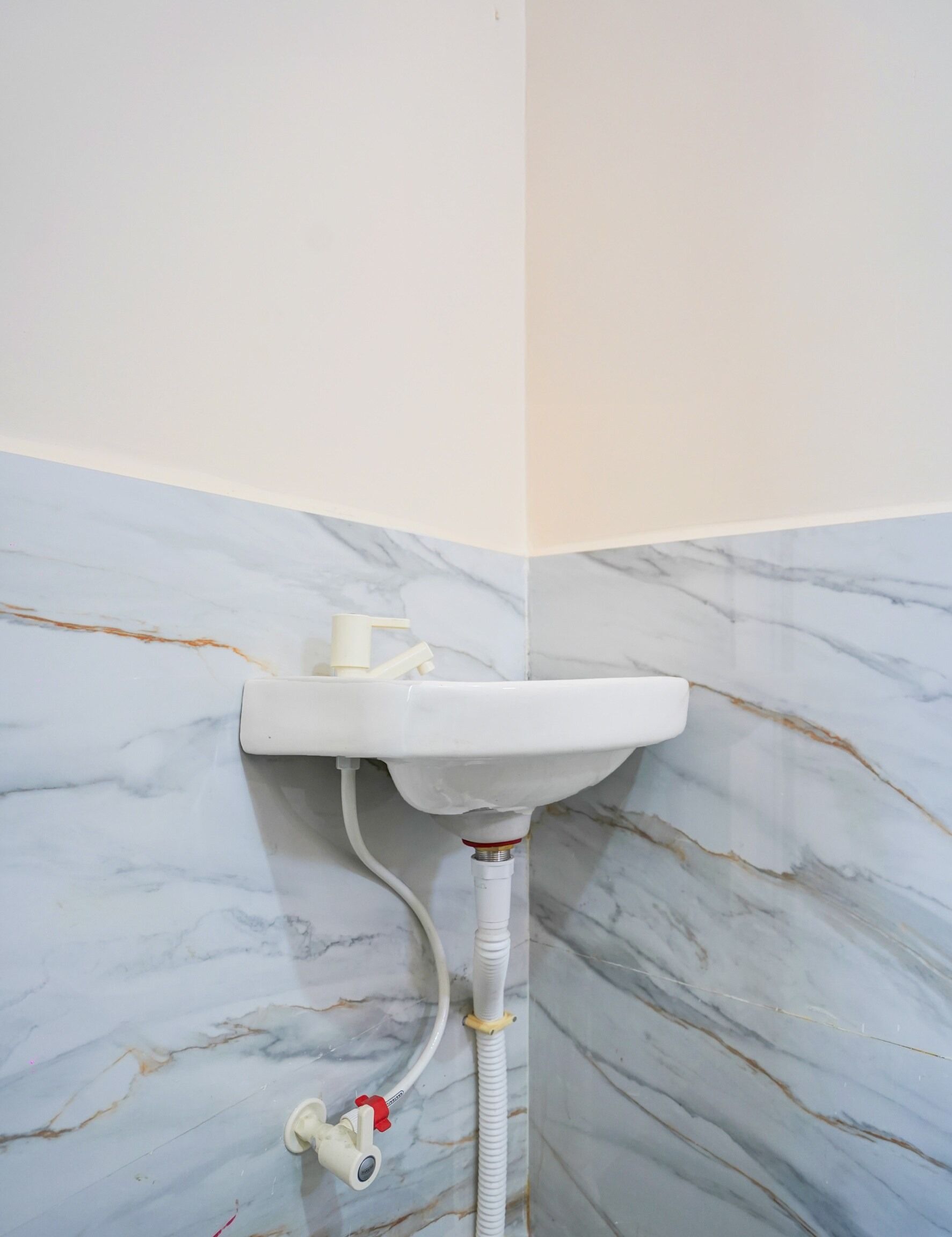 A bathroom with a white pedestal sink, marble walls, and a visible pipe.