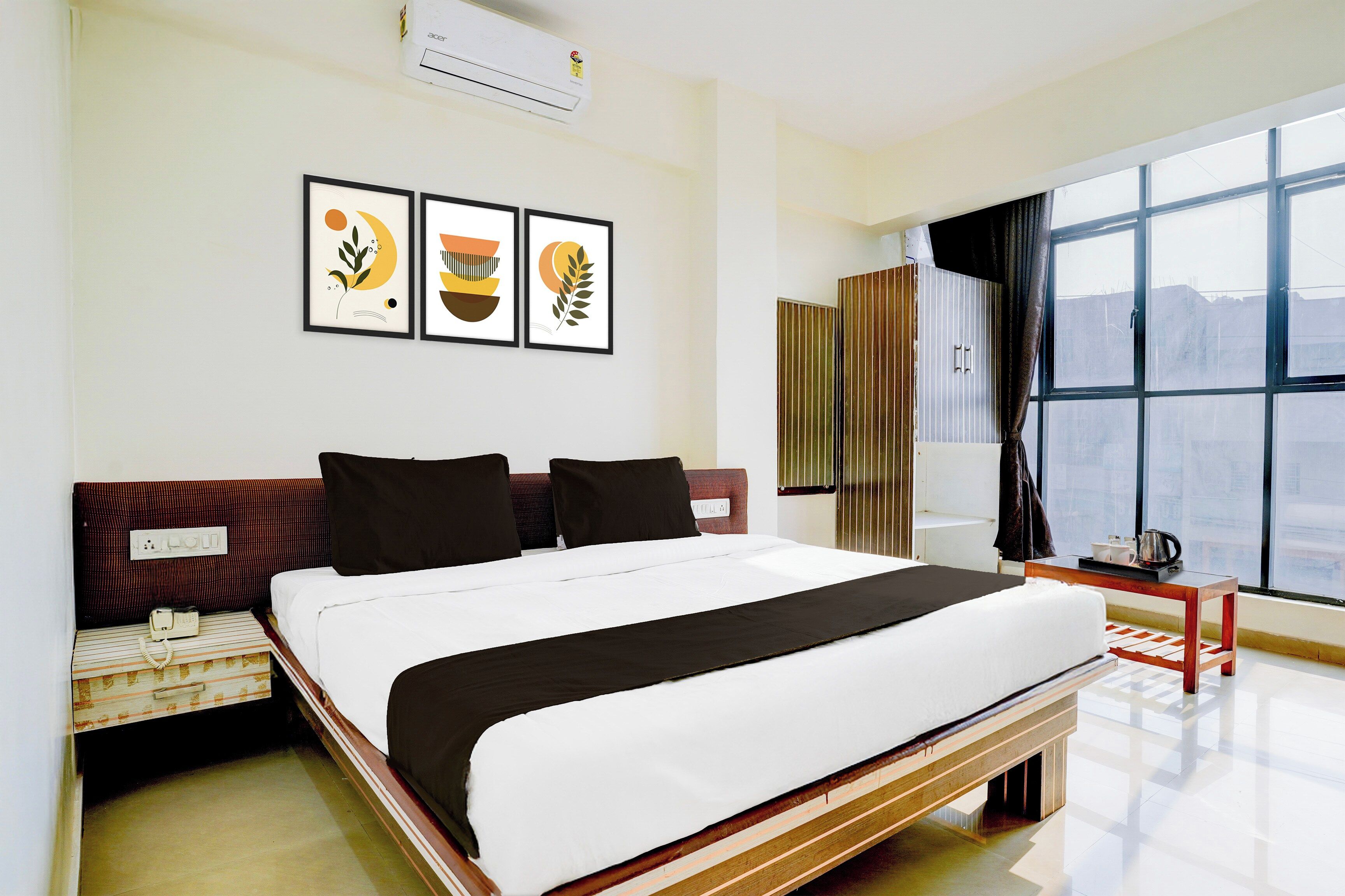 A hotel room with a bed, a bedside table, a window with curtains, and wall art.