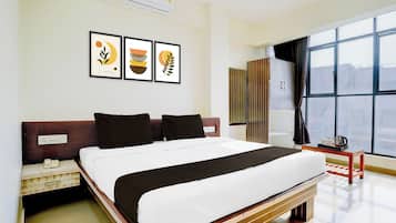A hotel room with a bed, a bedside table, a window with curtains, and wall art.