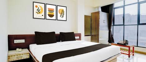 A hotel room with a bed, a bedside table, a window with curtains, and wall art.