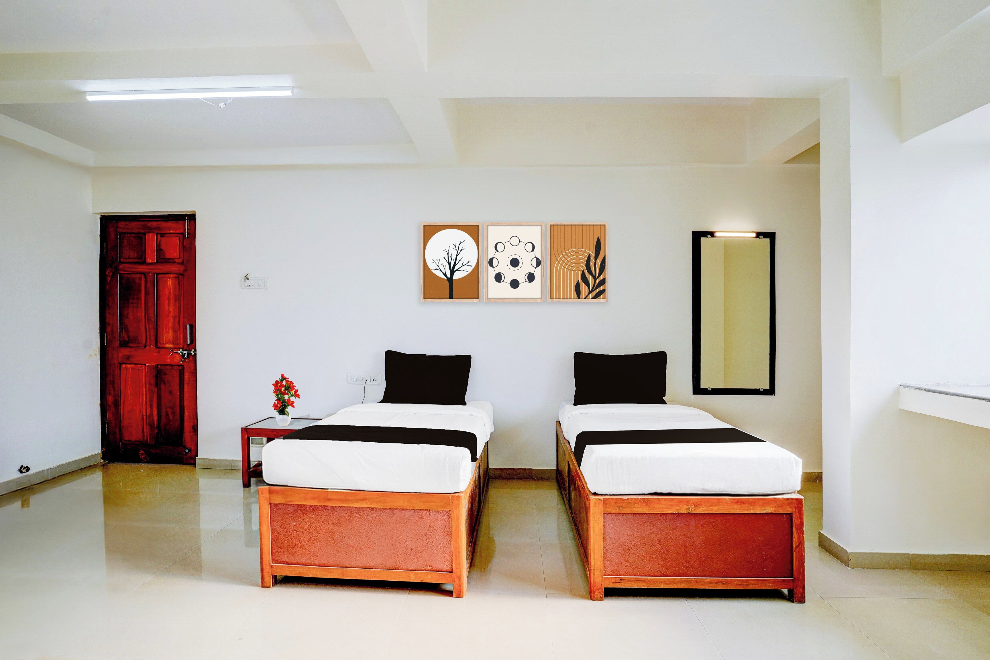 A hotel room with two beds, a wooden floor, a red door, and wall art.