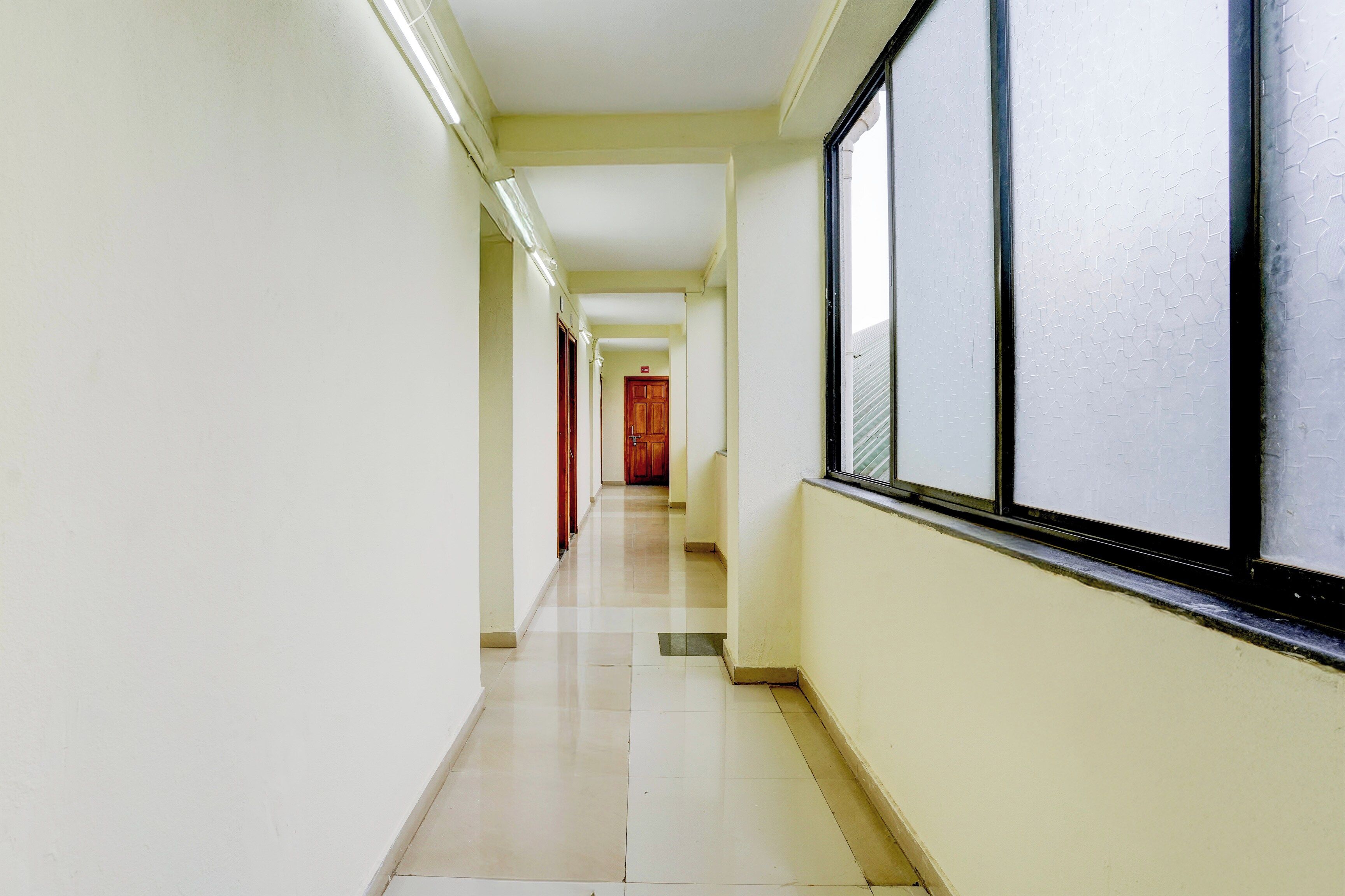 Un pasillo con piso de baldosas, una ventana con diseño en relieve y una puerta de madera al final.